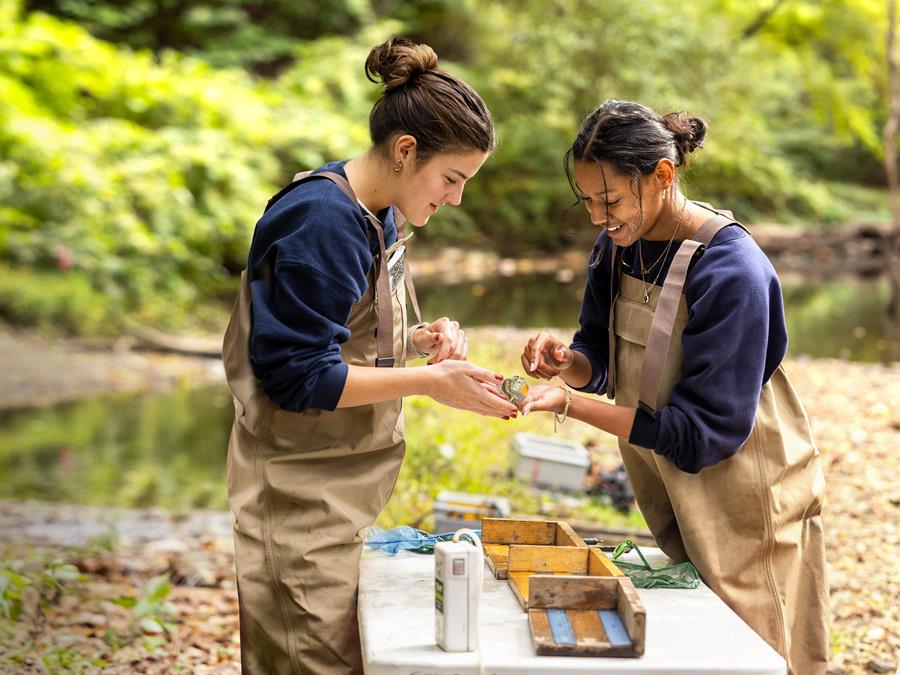 Two female students examine fossils by a creekbed