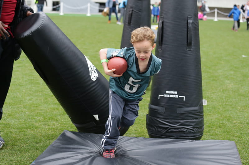 A boy in an Eagles jersey running through tackling dummies.