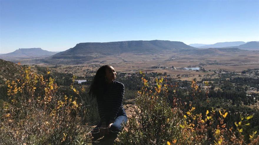 Woman sits in field with mountain in background.
