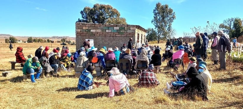 A group of people sitting outside next to a stone structure.