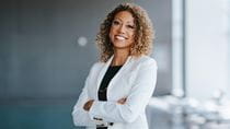 An image of Angela Val in white blazer standing with her arms crossed.