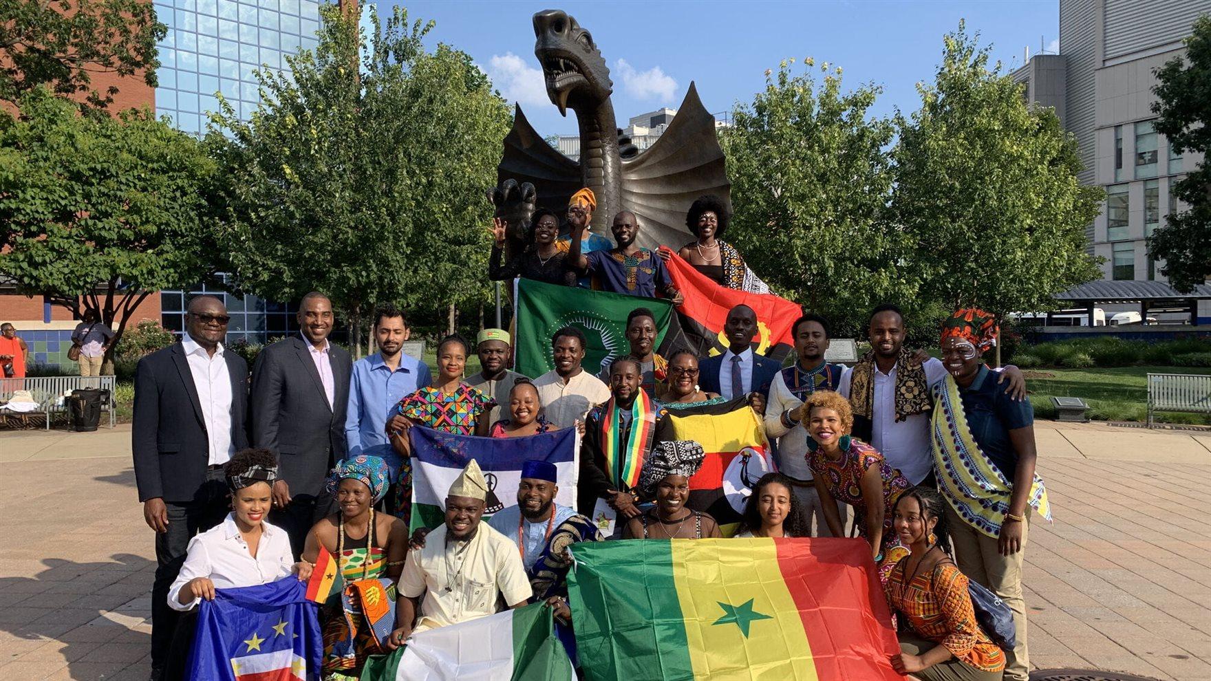 Two rows of people standing in front of the dragon statue on Drexel's campus holding flags of their home African countries.