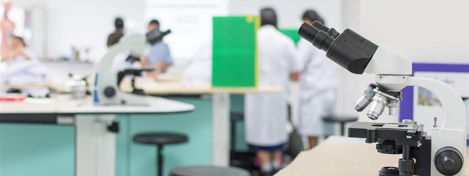 Microscope in a lab with people in lab coats in background