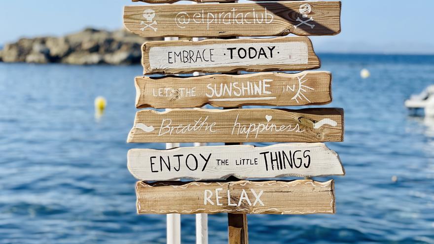 Wooden signs stacked on a beach with different sayings related to enjoying the moment.