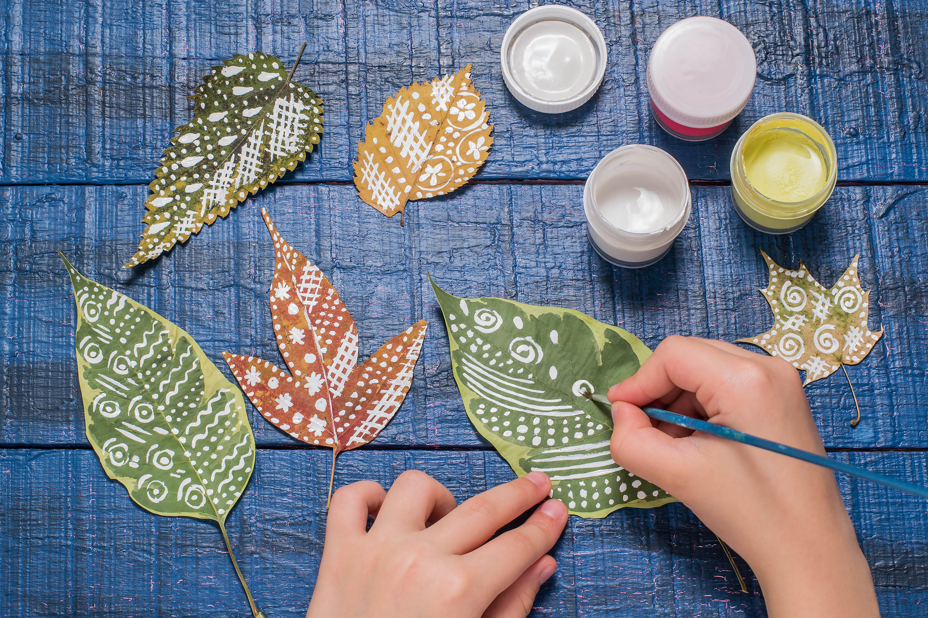 hands holding a paintbrush painting leaves
