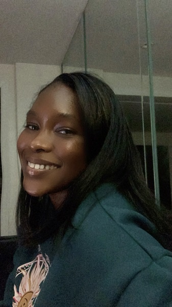 Smiling Black female with shoulder-length dark hair wearing a dark sweater with sun embroidery on the front