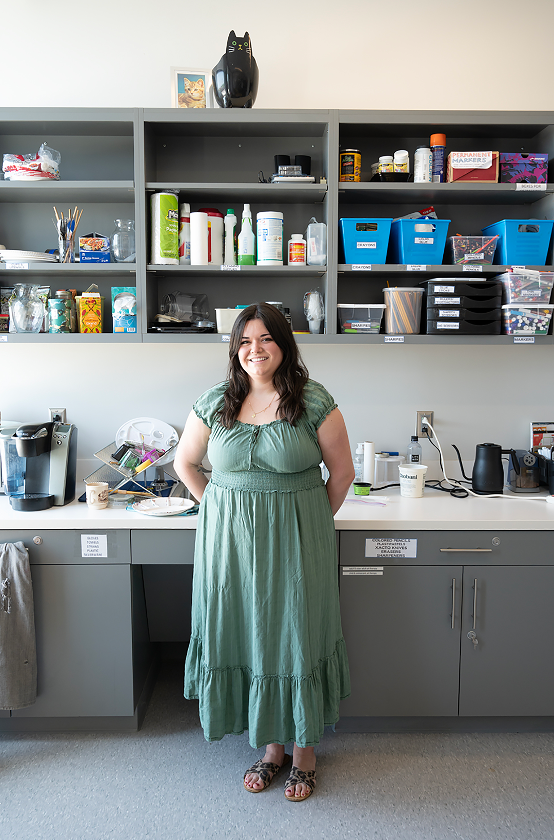 Morgan stands in front of CAT studios cabinets, full of various art supplies. 