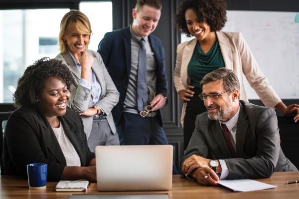 group of professional adults standing around a computer and smiling