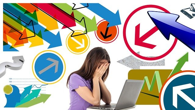 Image of a business woman with her head in her hands with many colorful arrows pointing at her.