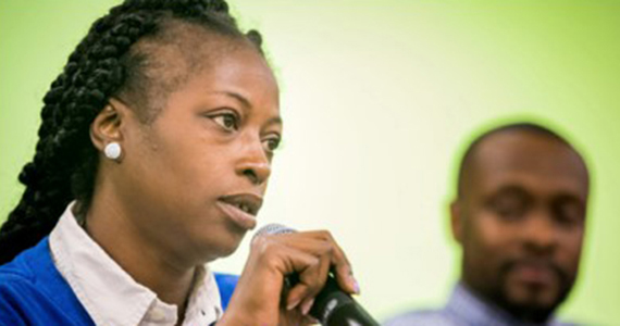 Black woman speaking on microphone with man behind her