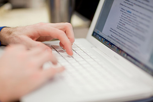 Close-up photo of hands typing on a laptop computer. Part of the laptop screen is in view.