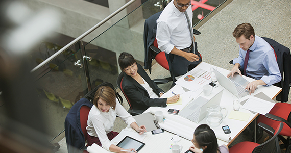 Female professor speaking to group of students at table 