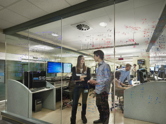 Two individuals speaking behind a glass wall with notes written on it 